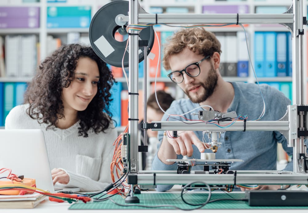 Engineer students in a lab internship discuss a machine.